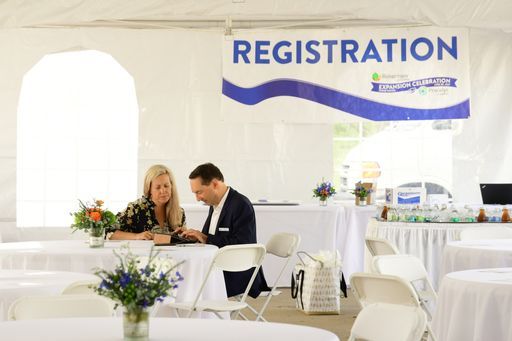 A man and a woman are sitting under a tent under a sign that says registration