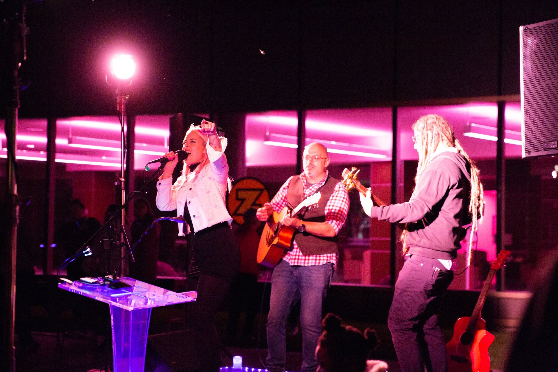 A woman singing into a microphone while two men play guitars on stage