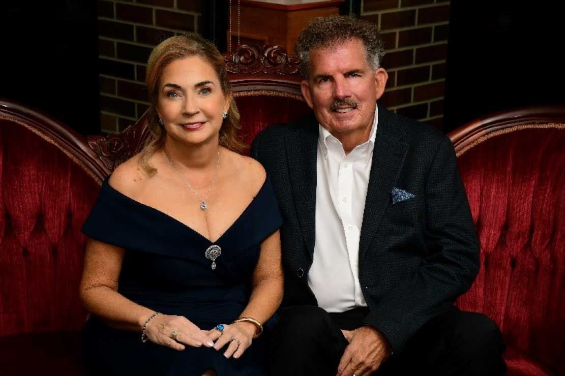 couple seated on red velvet couch; woman in blue dress, man in dark jacket