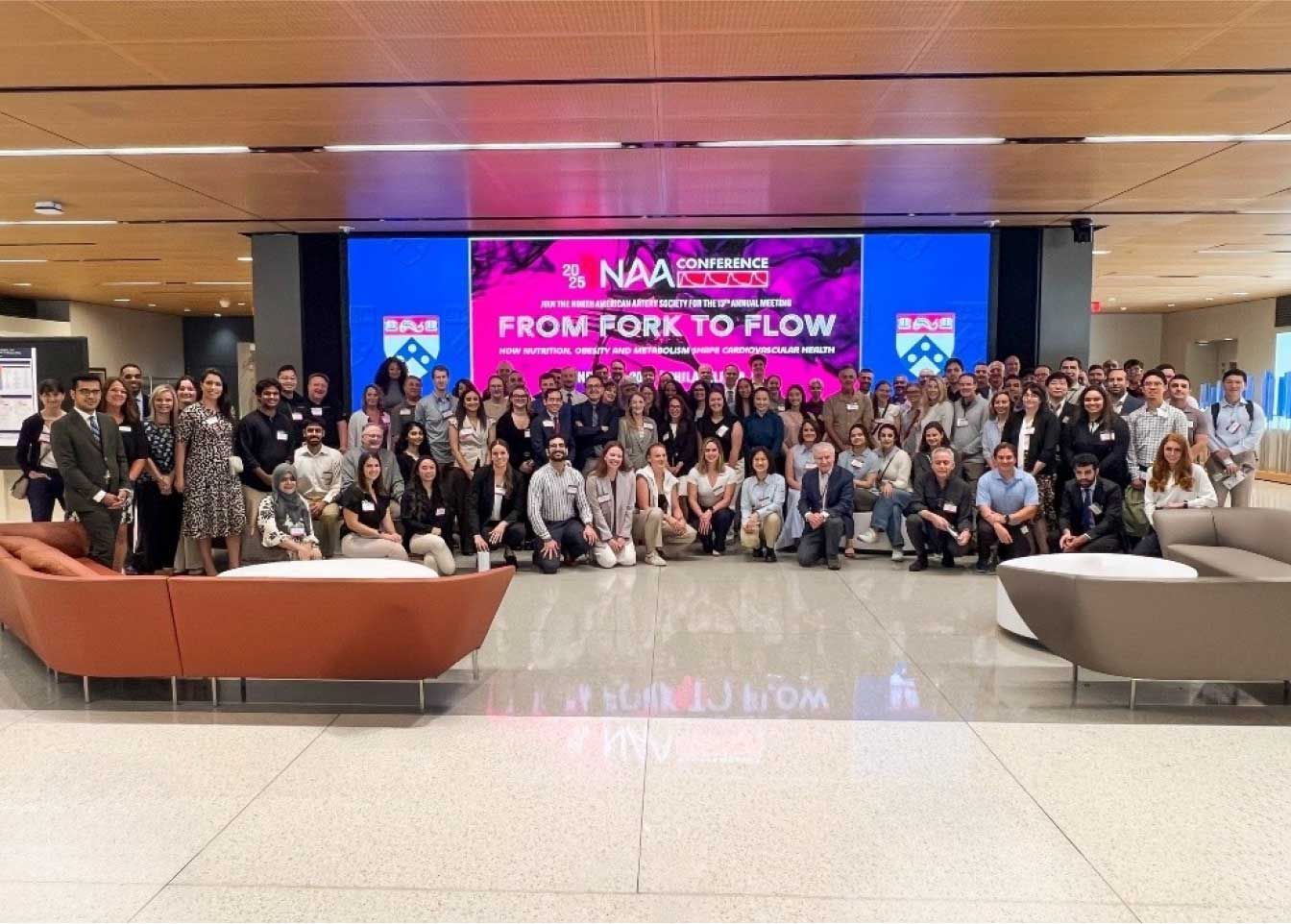 large group of people posing together in a modern building with a large screen