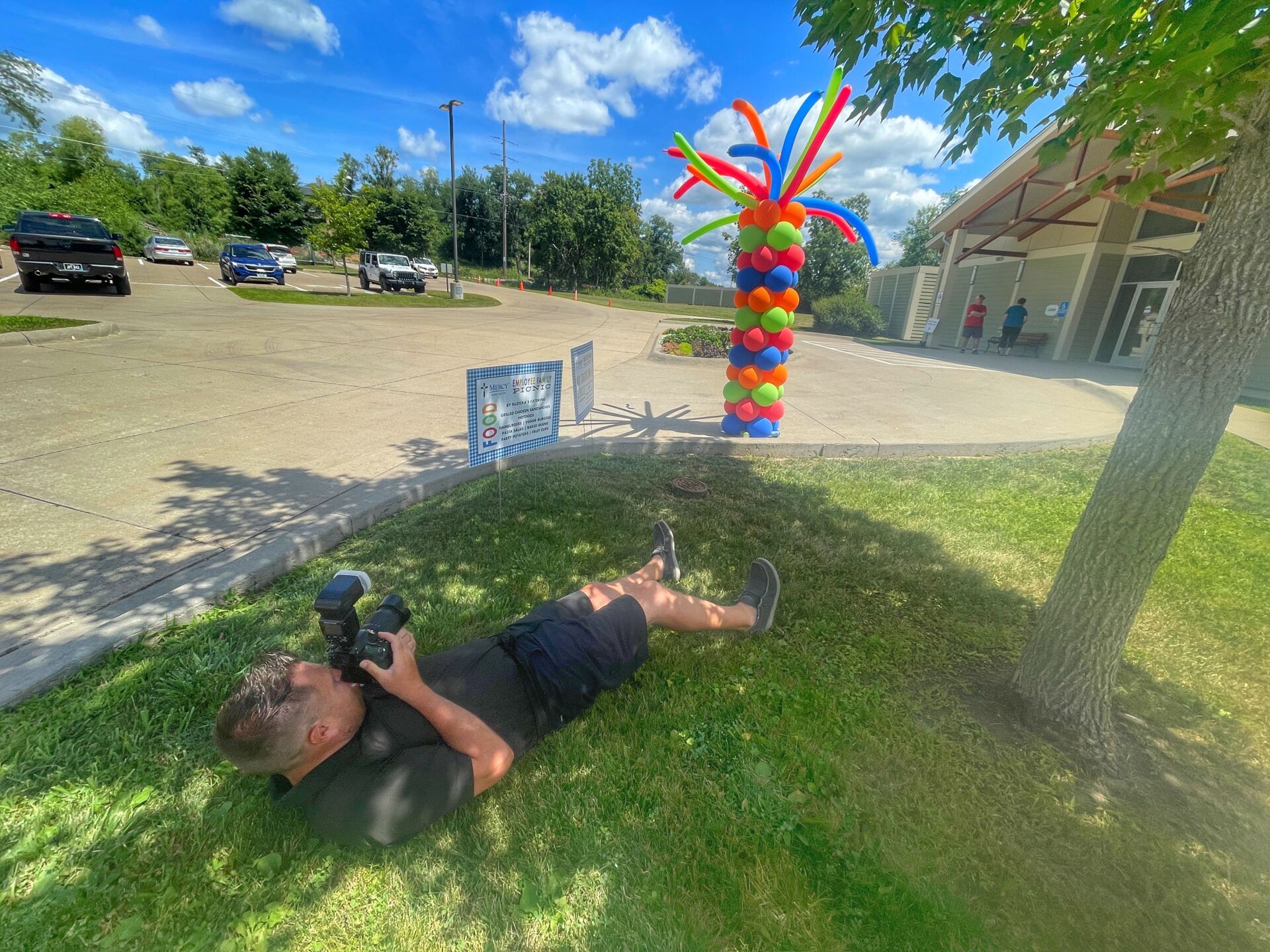 A man is laying on the grass taking a picture of a balloon display.