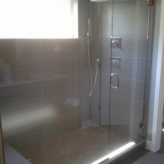A bathroom with a walk in shower with a glass door and a window.