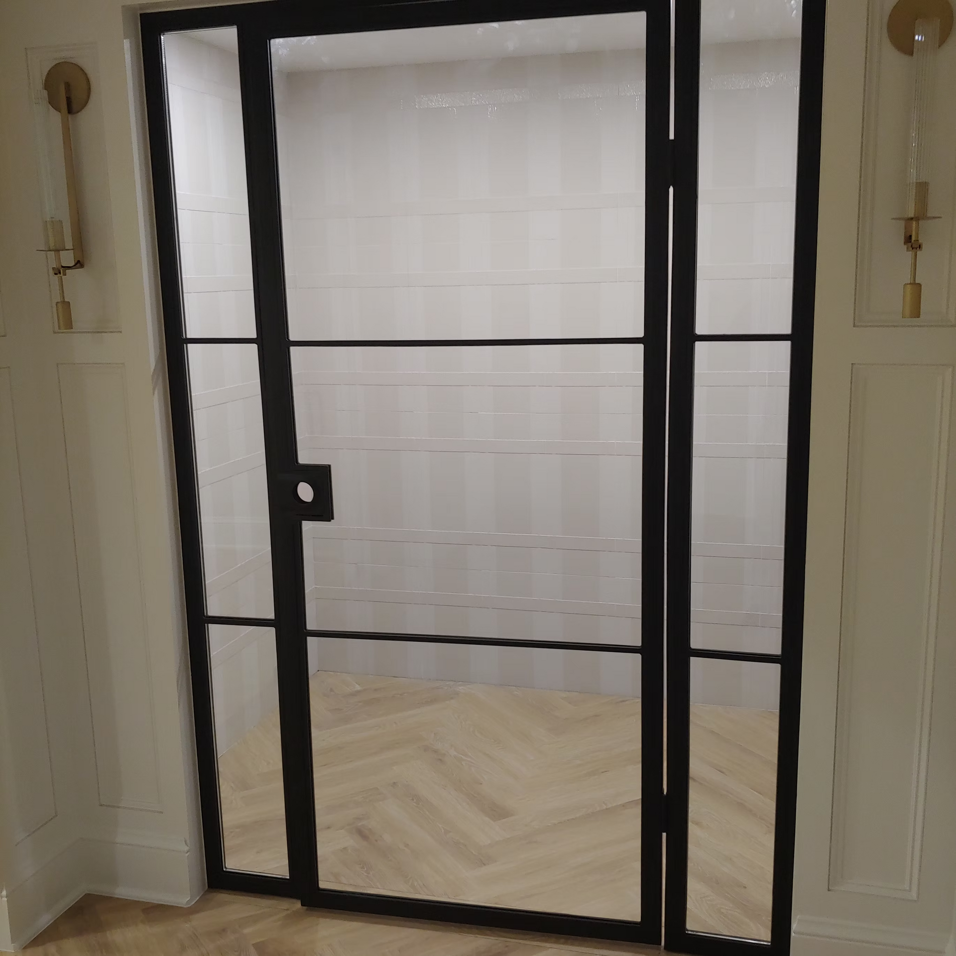 A door with a black frame and glass in a room with a herringbone floor.