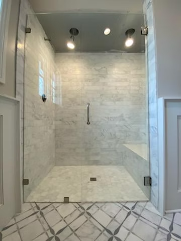 A bathroom with a walk in shower with a glass door.