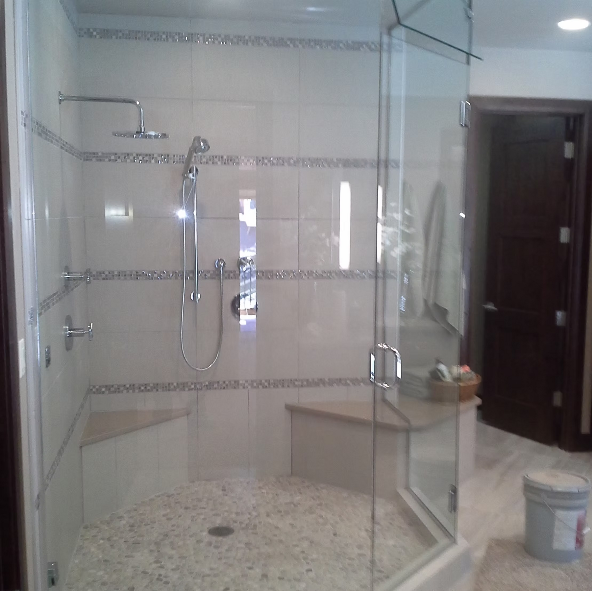 A bathroom with a walk in shower and a bucket on the floor