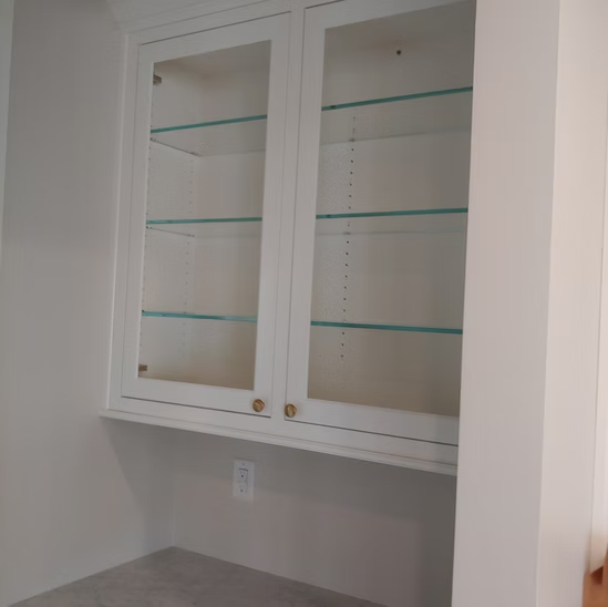 A white cabinet with glass doors and shelves in a room.