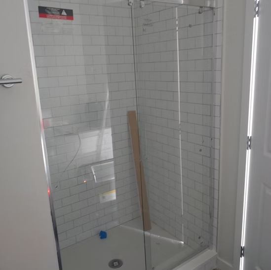A bathroom with white tiles and a glass shower door.