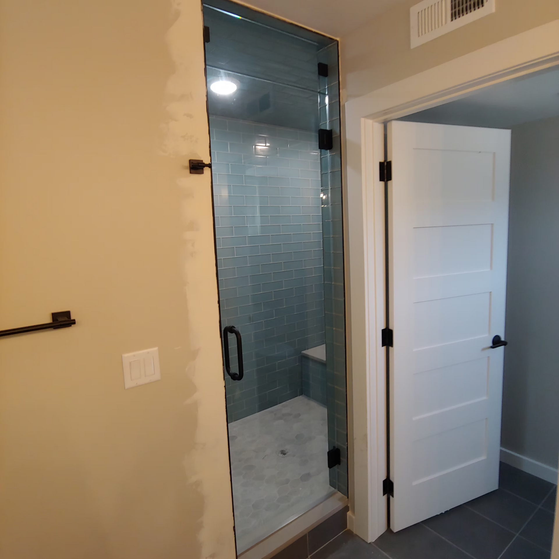 A bathroom with a glass shower door and a white door