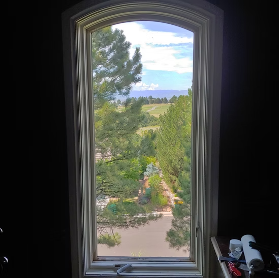 A window with a view of a forest and mountains in a dark room.
