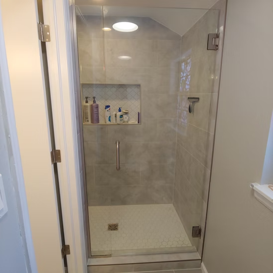 A bathroom with a walk in shower with a glass door.