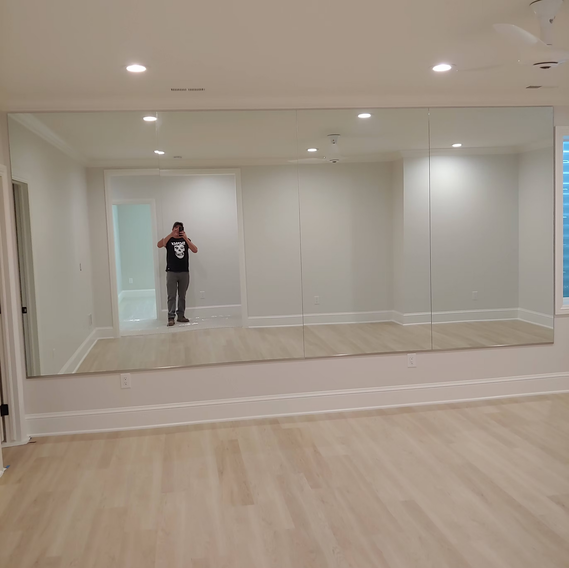 A man is standing in front of a large mirror in a room.