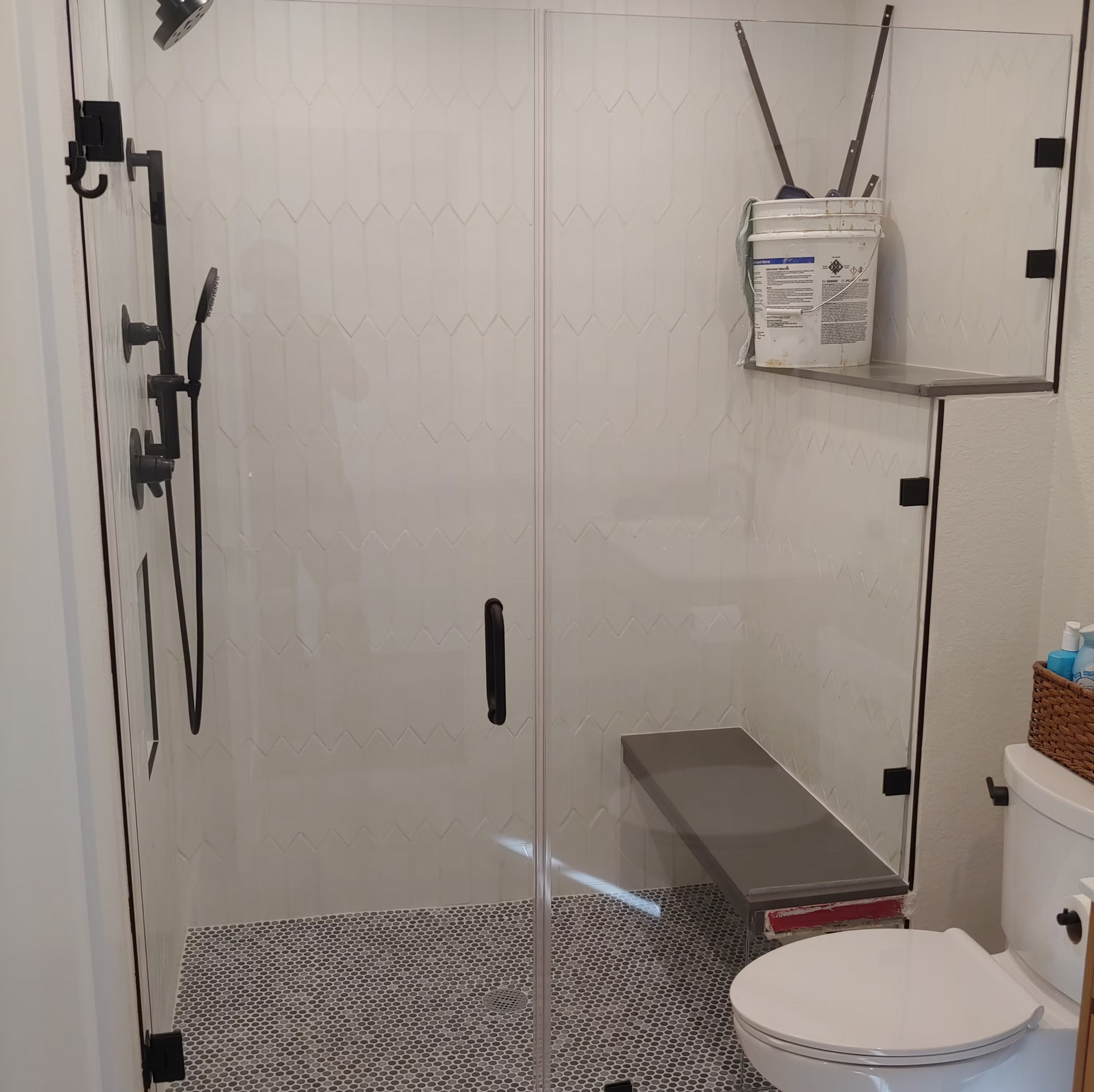 A bathroom with a toilet , shower , and bench.