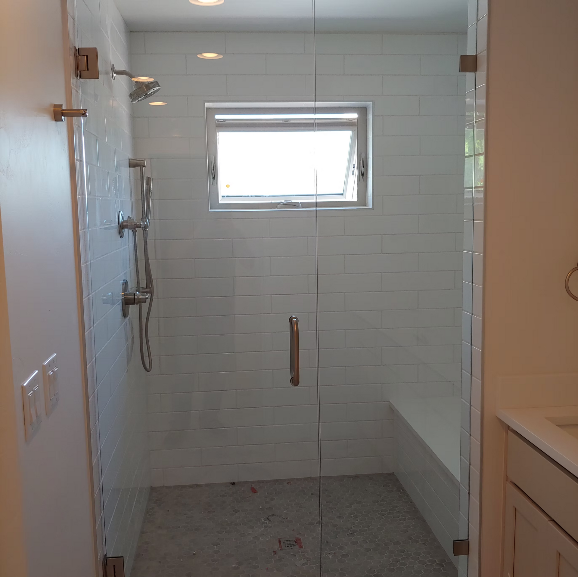 A bathroom with a walk in shower with a glass door and a window.