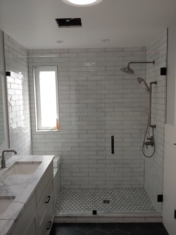 A bathroom with white tiles , a sink , a shower and a window.
