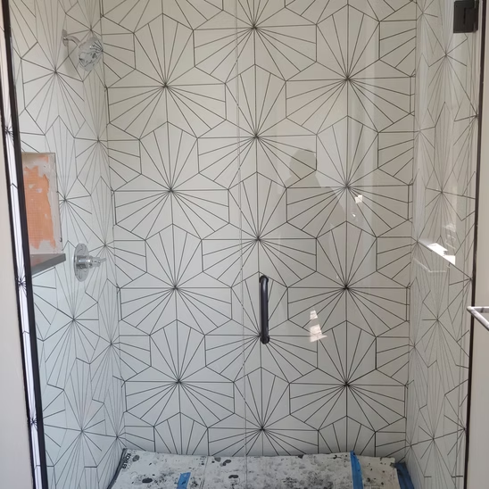 A shower with a glass door and white tiles on the wall.