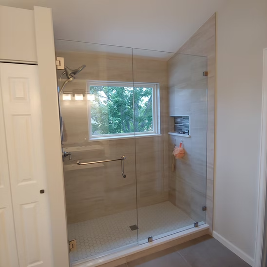 A bathroom with a walk in shower with a glass door and a window.