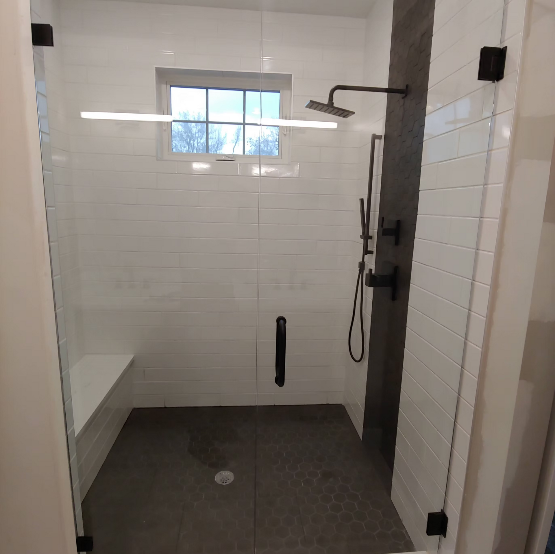 A bathroom with a walk in shower with a glass door and a window.