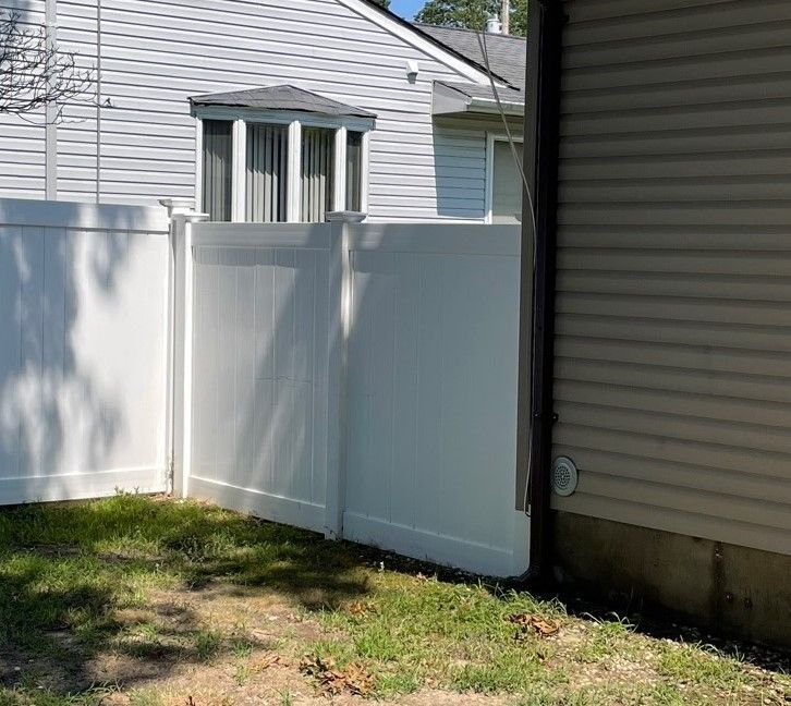 White vinyl fence covered in green algae; adjacent to a light brown house after.