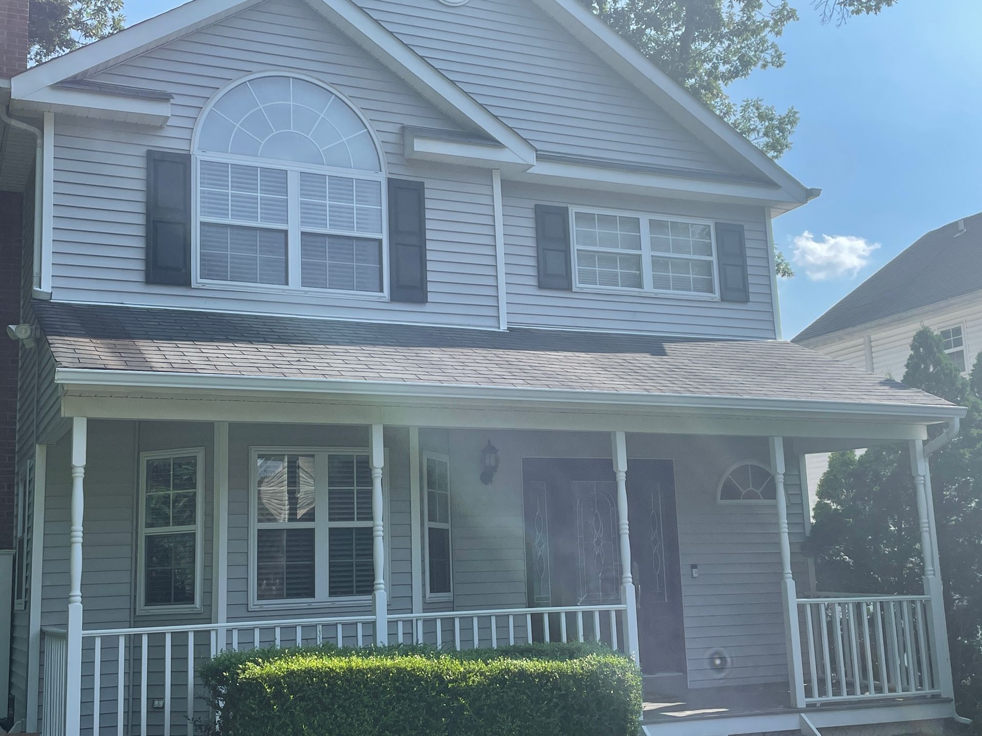 Two-story house with light gray siding, black shutters, and a covered porch under a bright blue sky after.