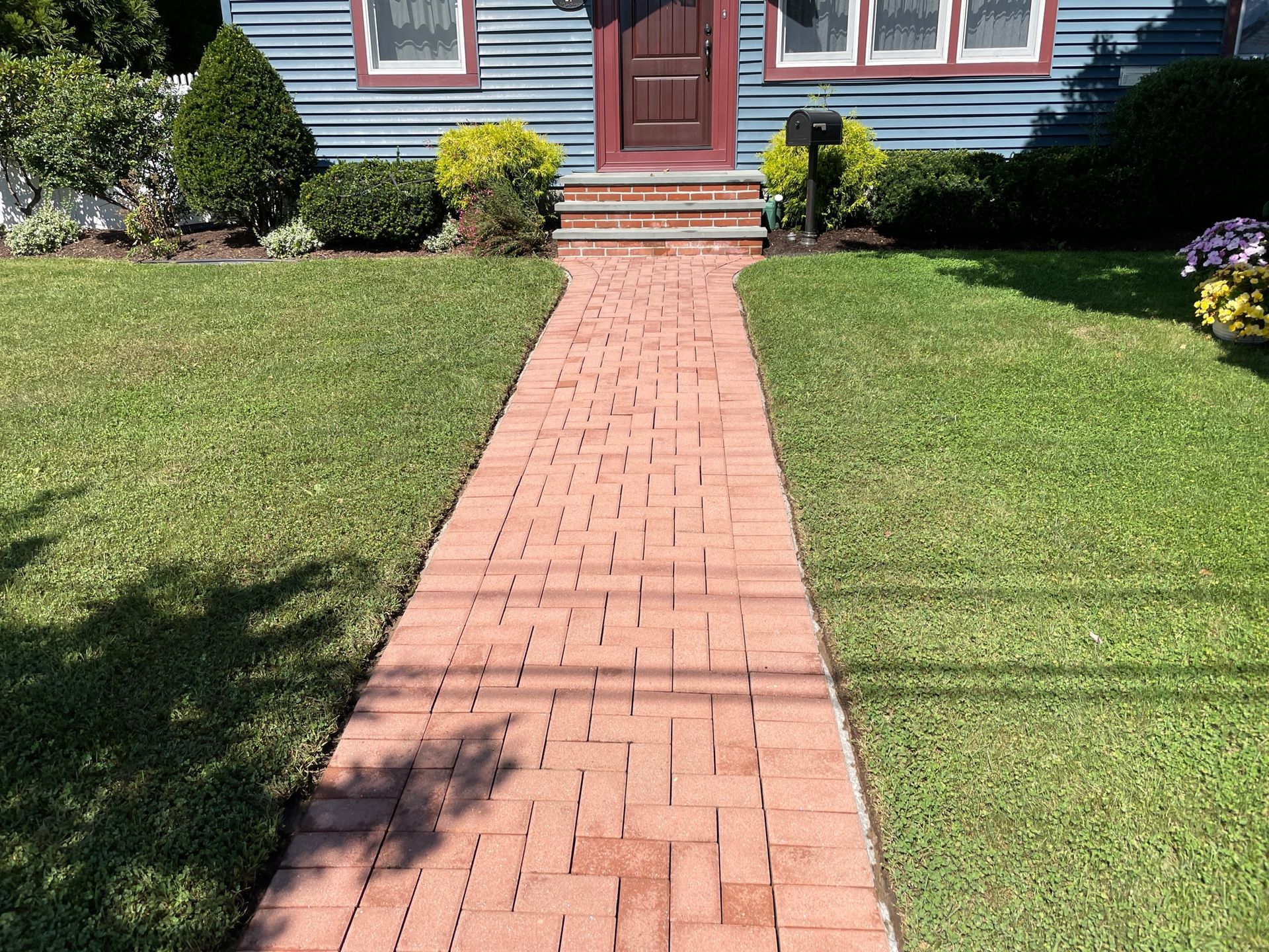 Brick path leading to a blue house with a brown door, steps, and green lawn after.