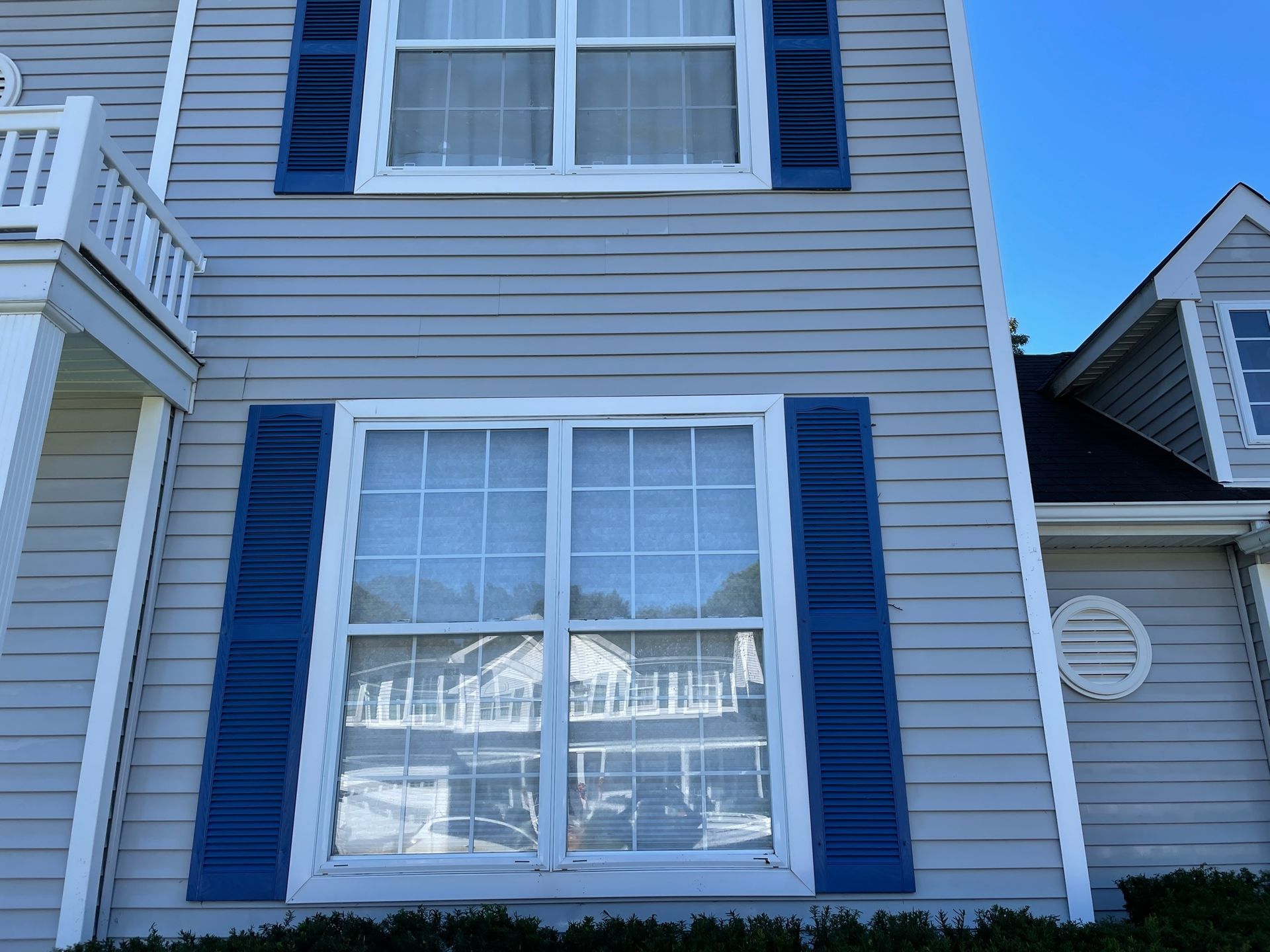 Two-story house exterior with blue shutters and weathered siding. Large arched window above a rectangular one after.