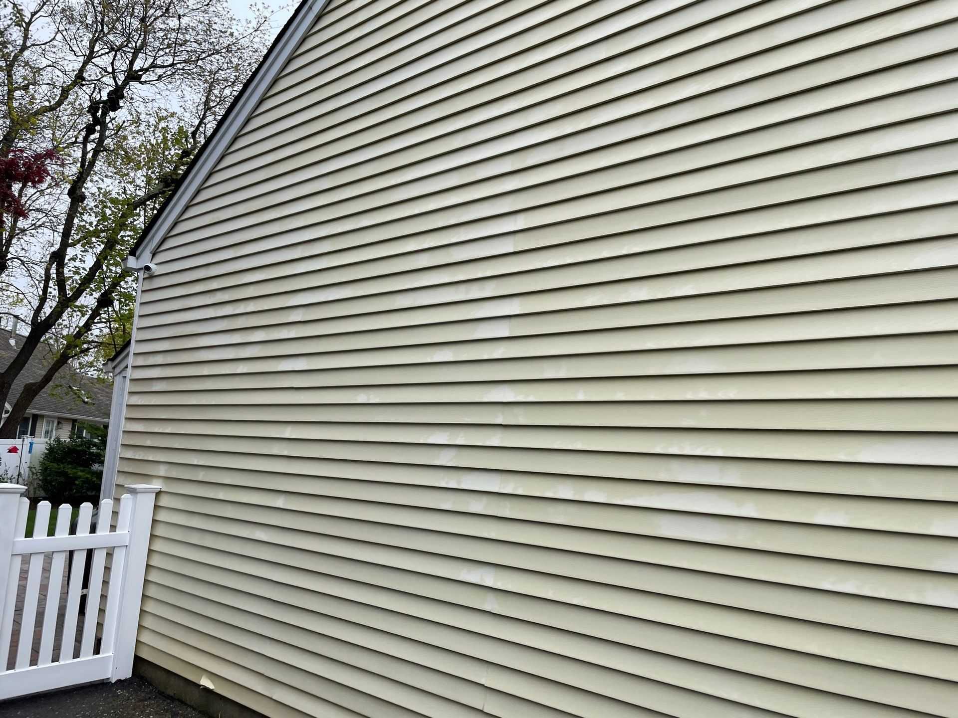Yellow house siding covered in grime, with a white fence and garage door visible after.