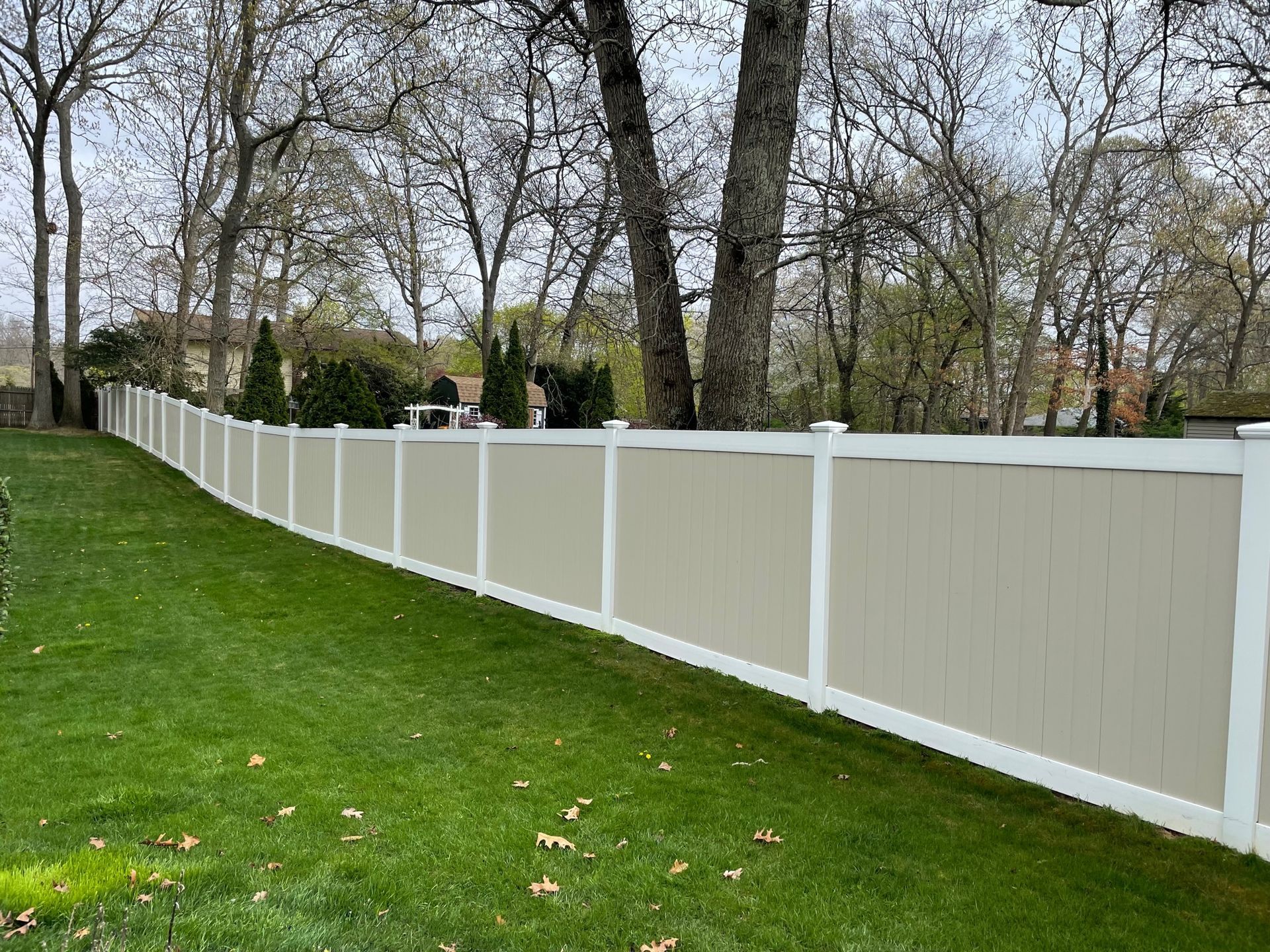 Beige vinyl fence along a green lawn, trees in the background after.