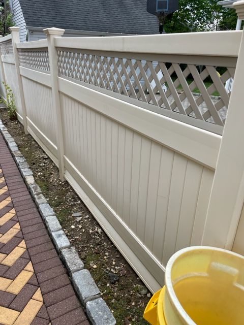 Cream-colored vinyl fence with lattice top along a brick paved driveway, showing discoloration from dirt and growth after.