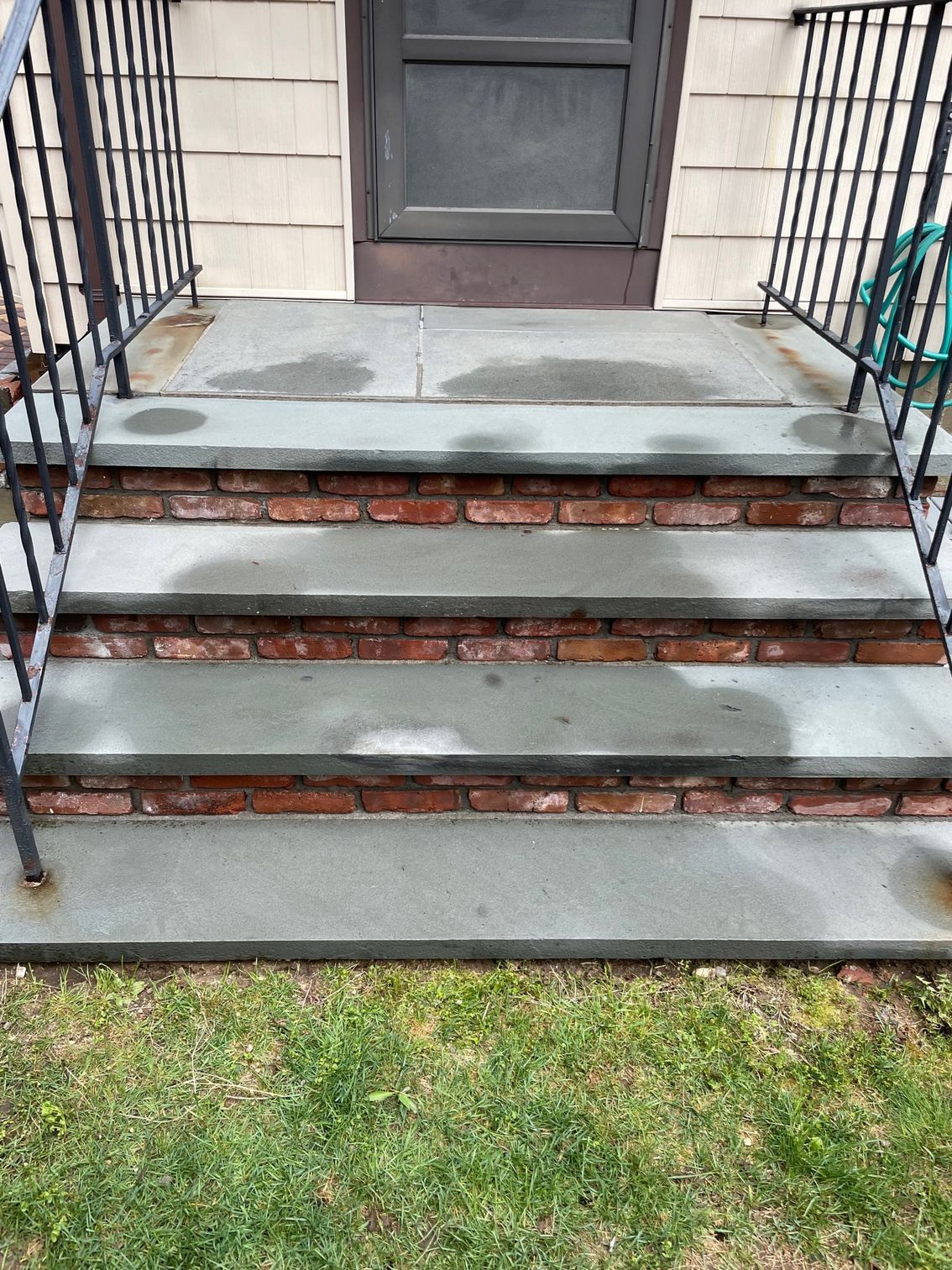 Concrete steps leading to a door with a welcome mat, set against a house with tan siding and a green hose after.