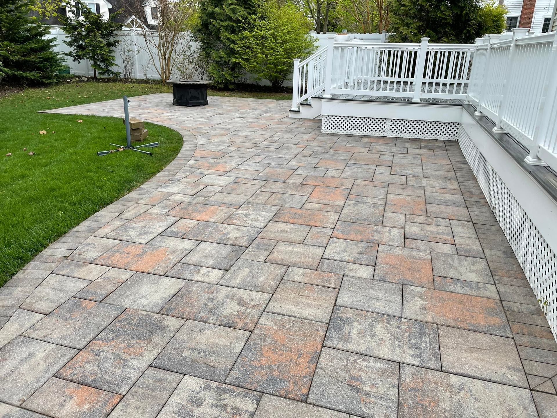 Brick patio next to a deck with white railings, and green grass after.