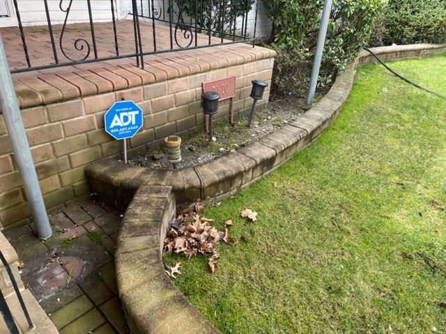 Brick home exterior with low brick retaining wall, grass, and security system sign before.