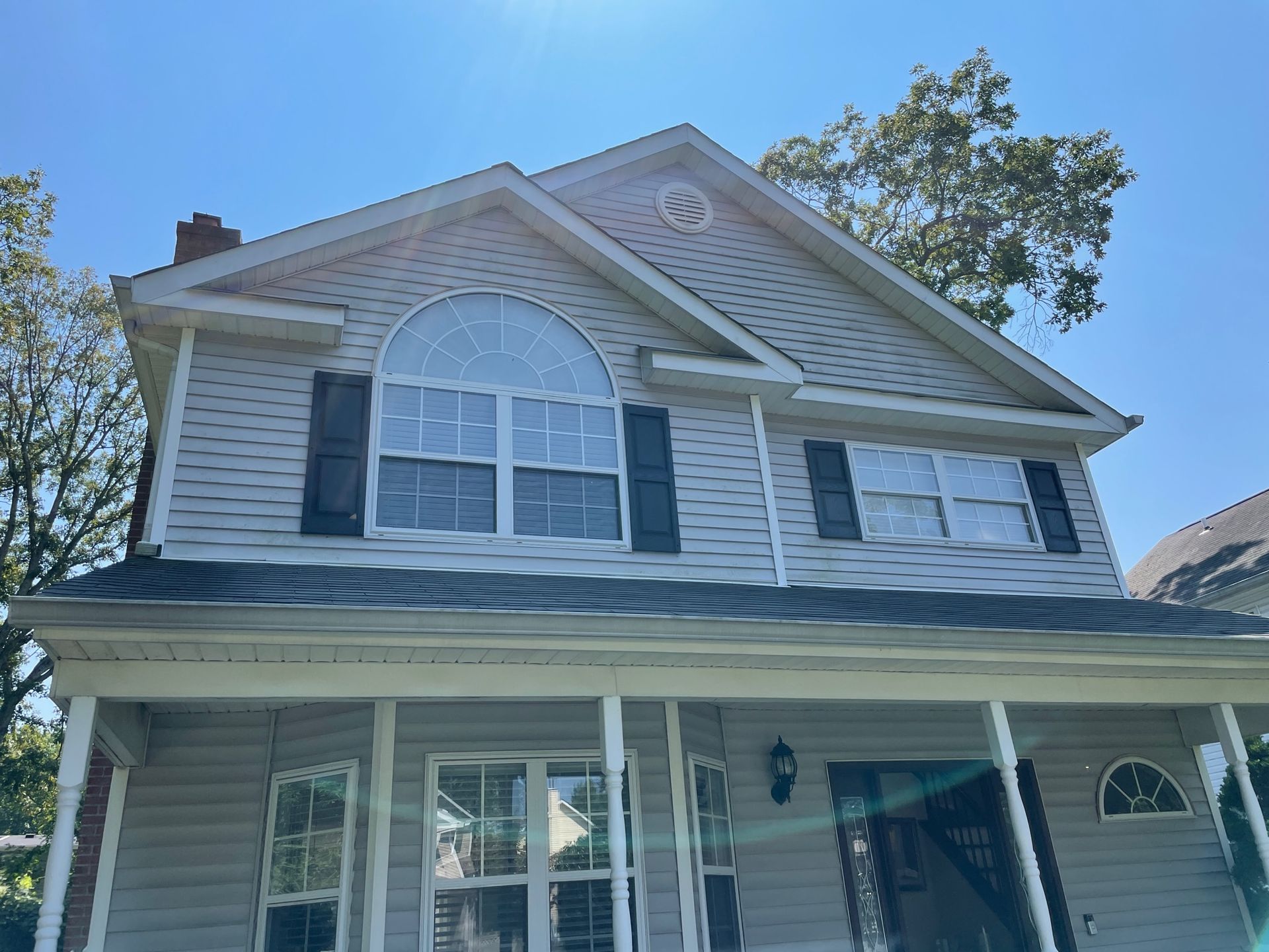 Two-story house with light gray siding, black shutters, and a covered porch under a bright blue sky before.