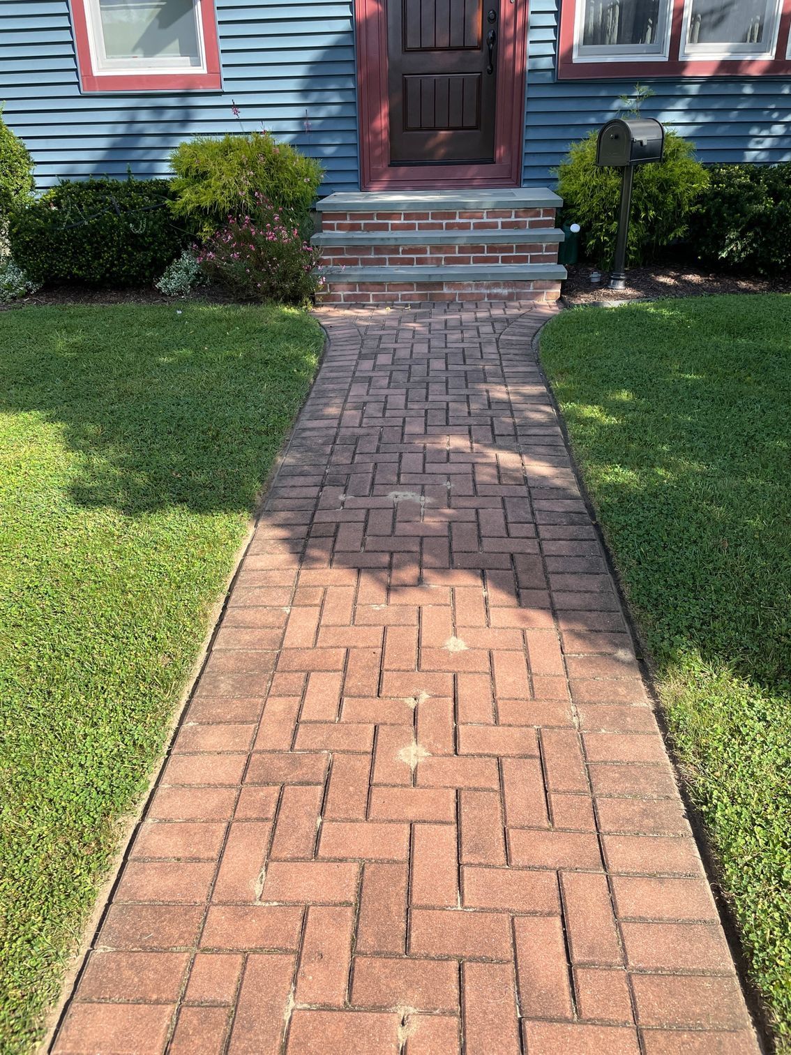 Brick path leading to a blue house with a brown door, steps, and green lawn before.