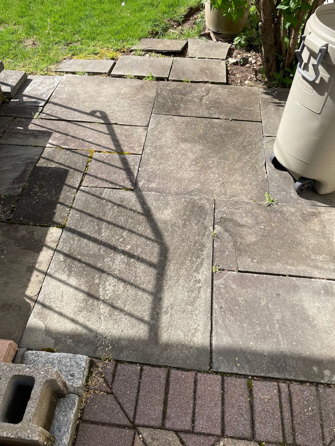 Stone path with a shadow from a railing; a rain barrel is visible before.