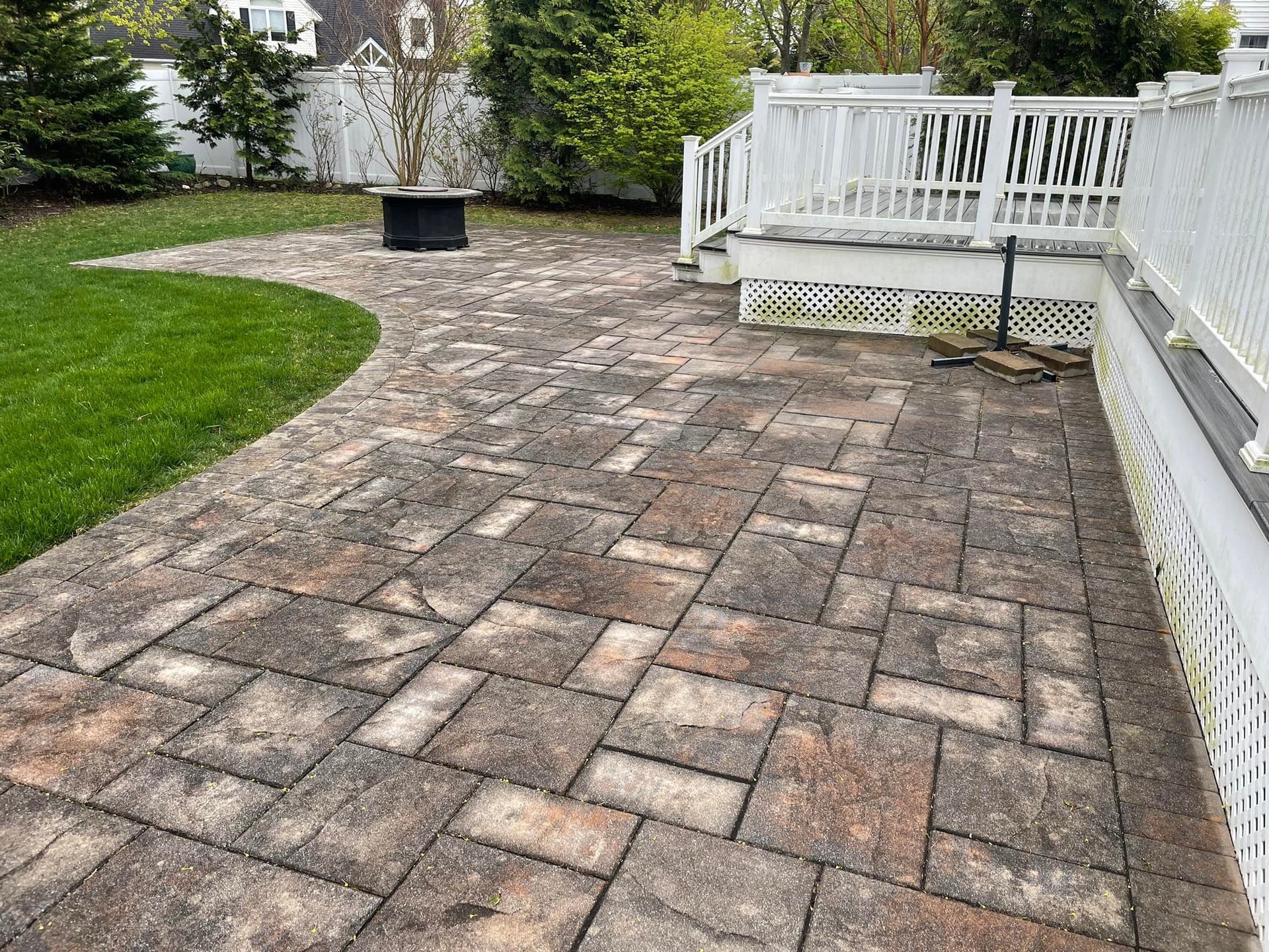 Brick patio next to a deck with white railings, and green grass before.