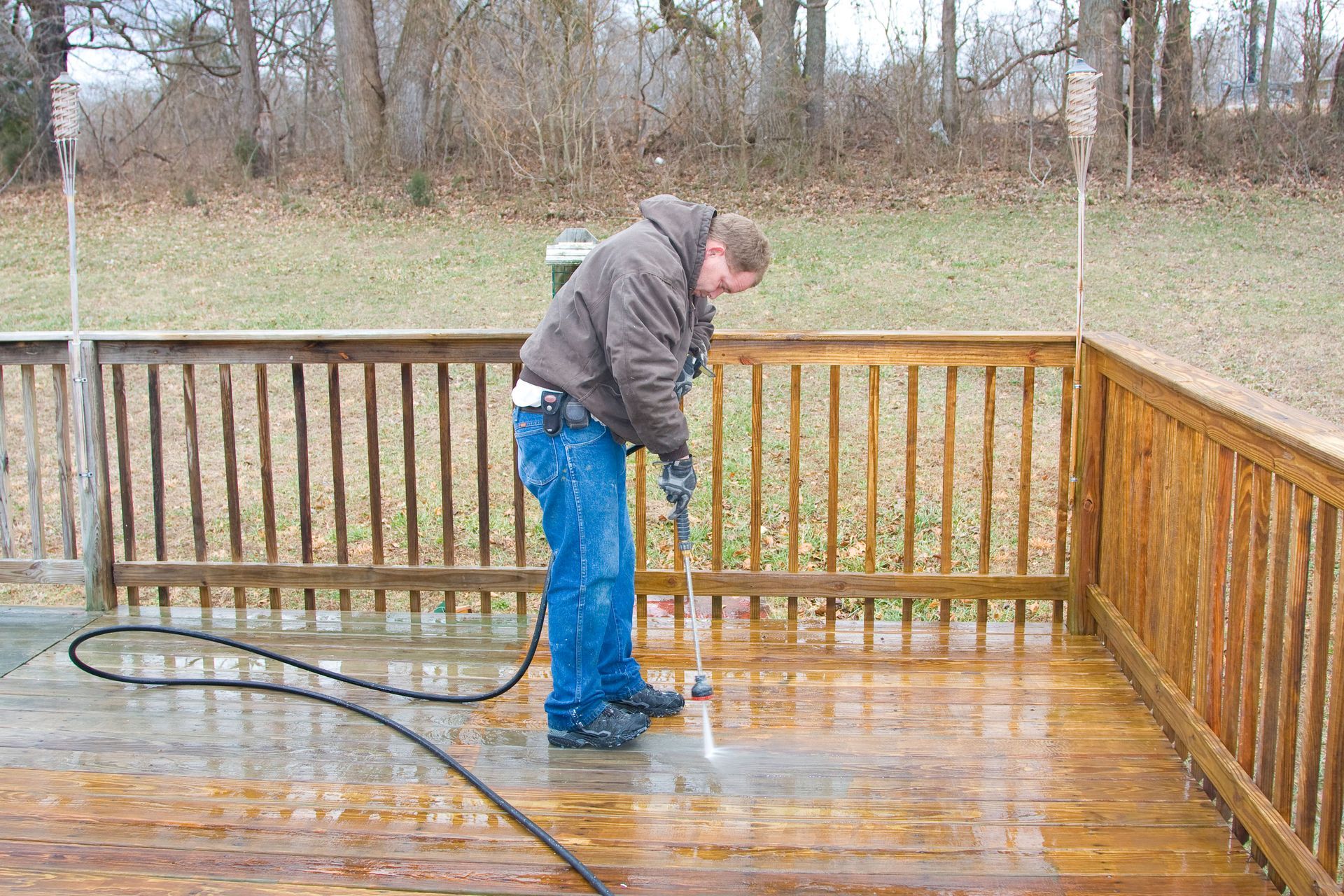 Man power washing a wooden deck outdoors.