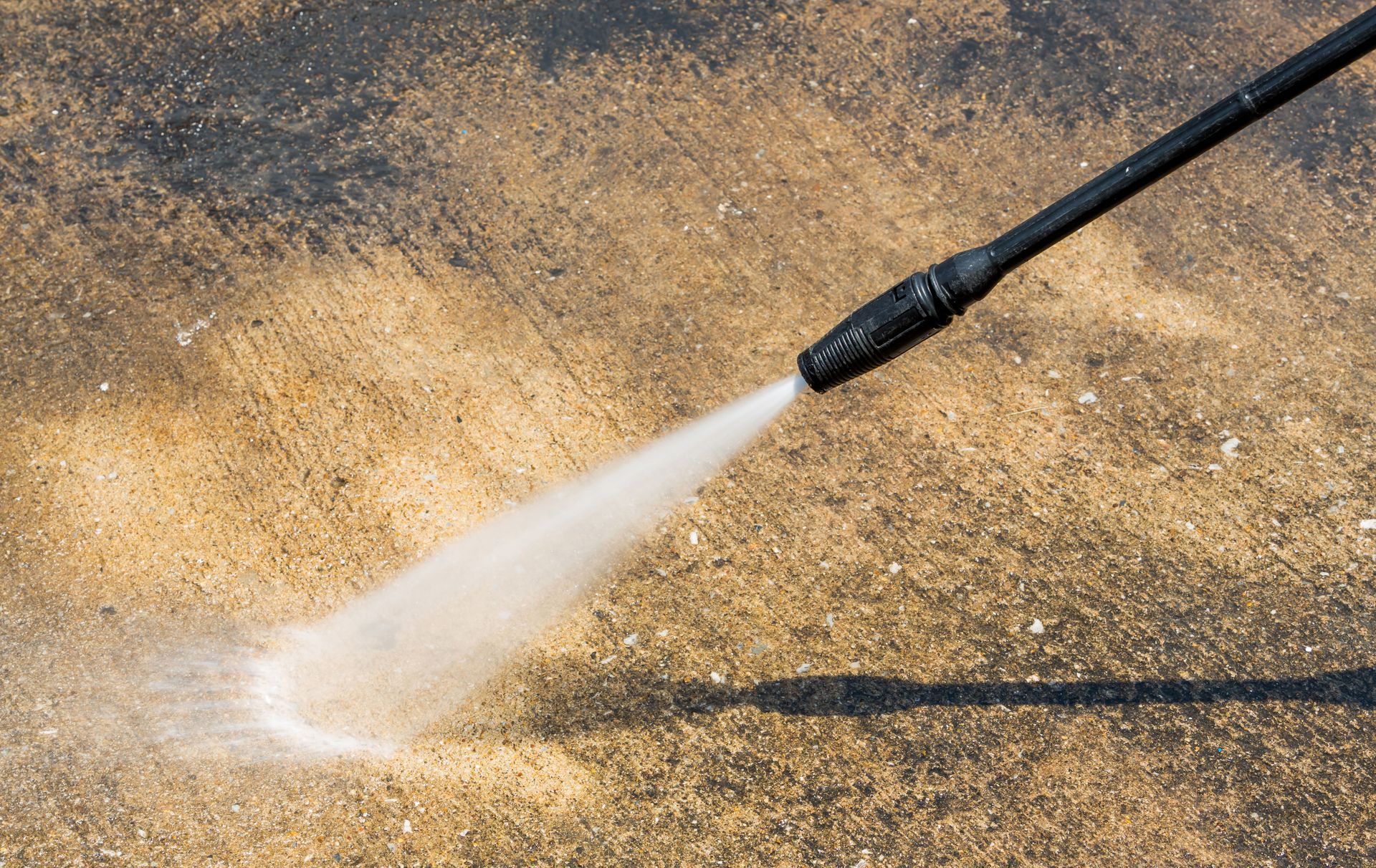 Pressure washer spraying water on a concrete surface, removing dirt and grime.