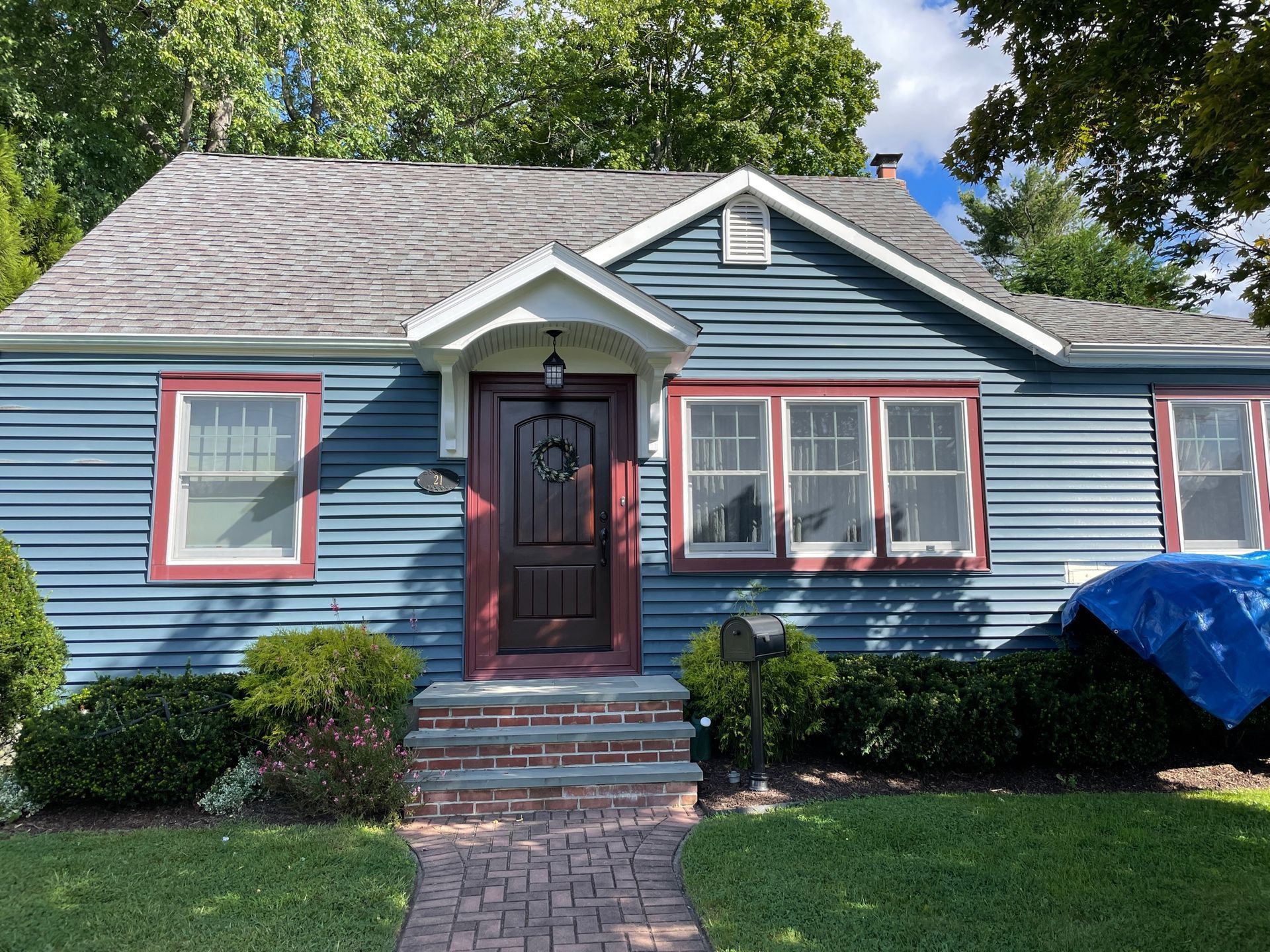 Blue house with red-trimmed windows and door. Brick steps lead to the entrance, and a blue tarp covers something on the right.