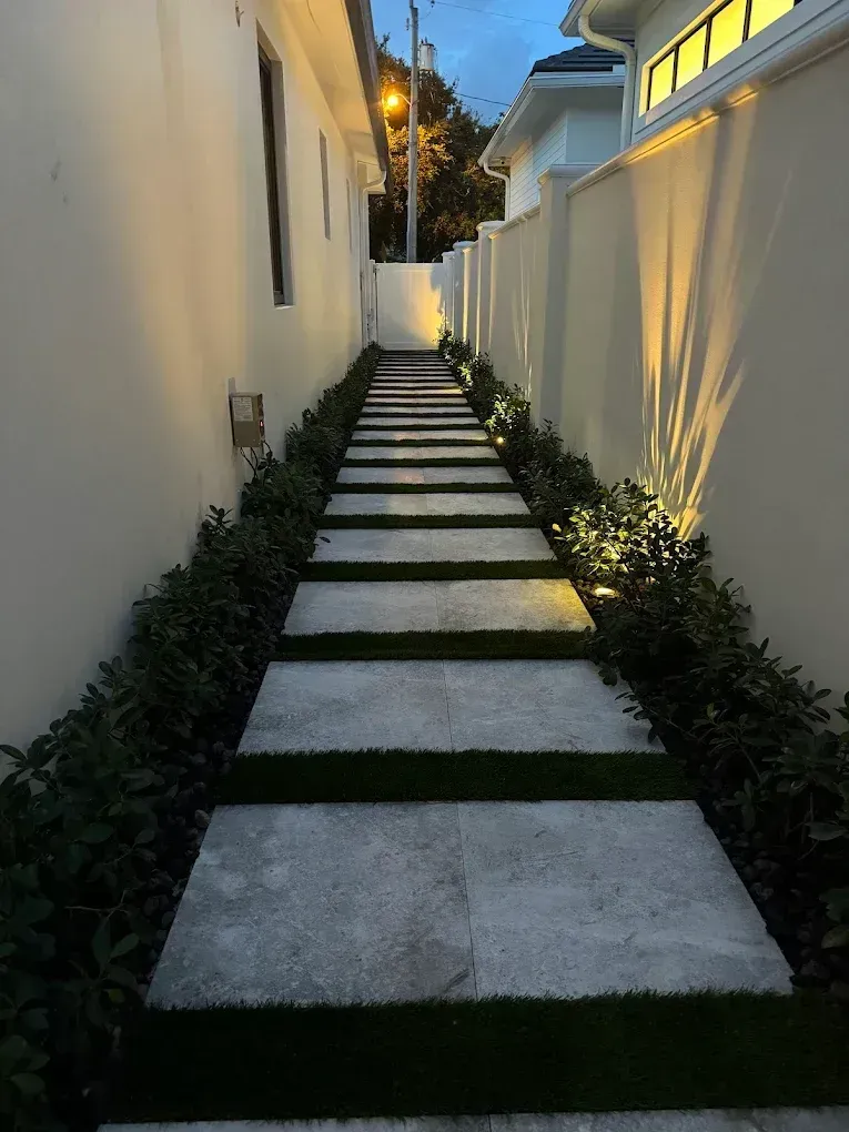 Stone pathway between walls, lined with greenery and illuminated by warm lights.