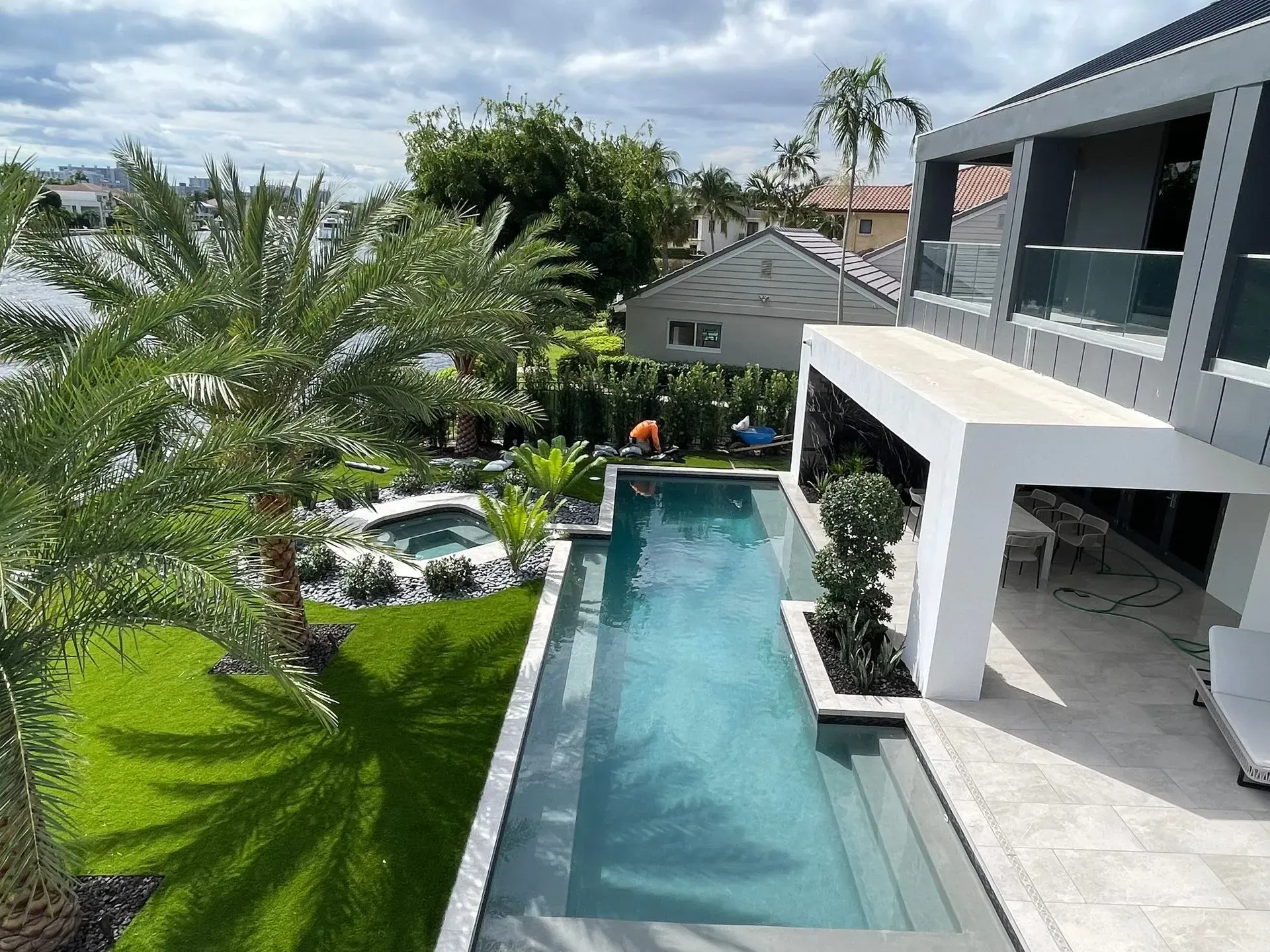 Modern home with rectangular pool, jacuzzi, and lush landscaping. Sunny day, bright blue water.