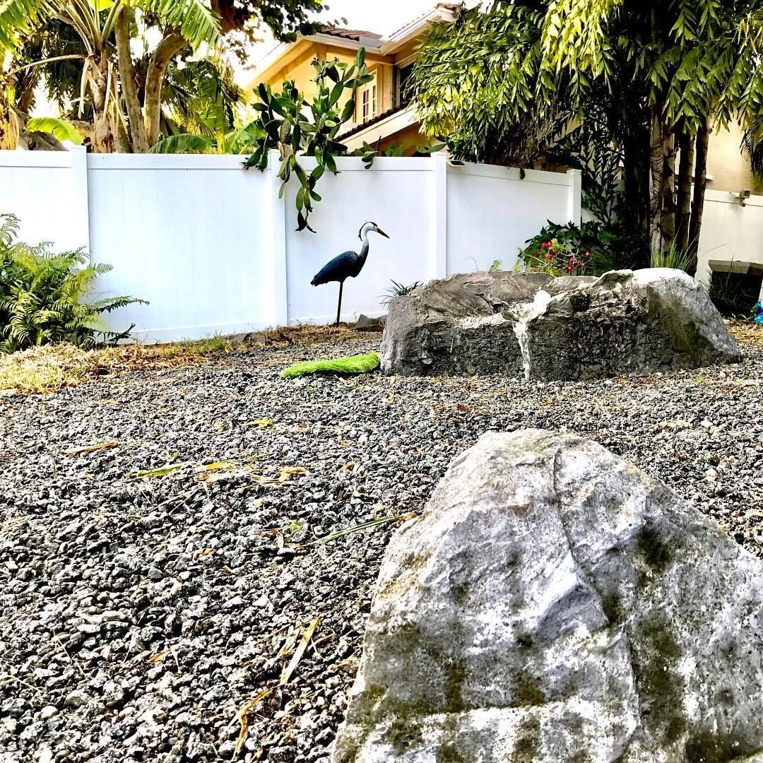 Gray rocks, a metal heron statue, and a white fence.