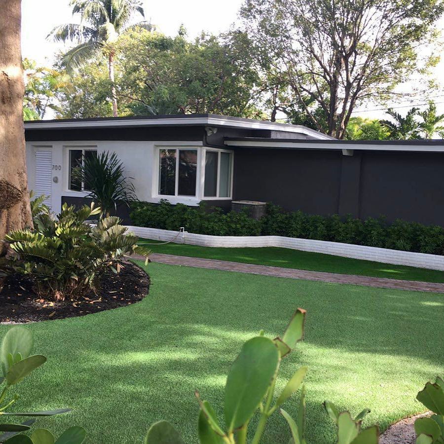 Modern white and gray house with black trim, green lawn, and lush landscaping.