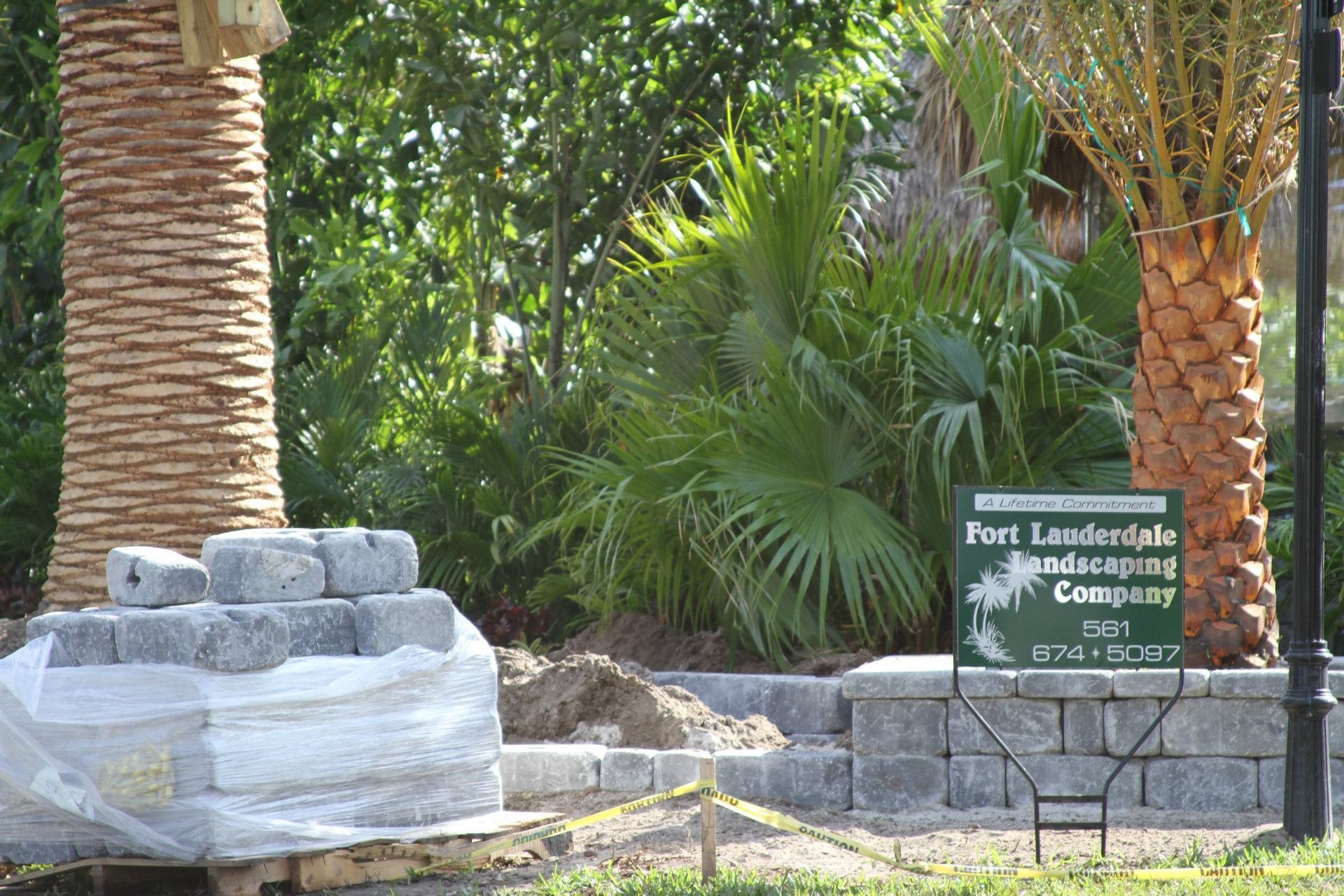 Landscaping scene: Palm trees, stacked stones, and a sign for "Fort Lauderdale Landscaping Company."