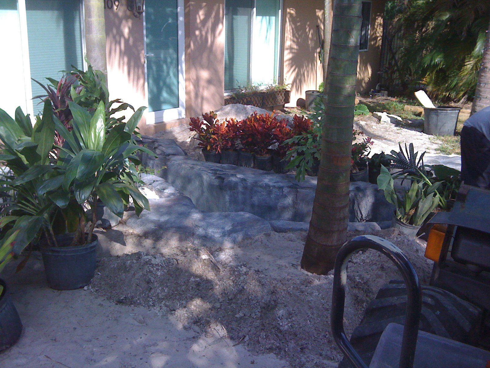 A garden with plants in pots, a small waterfall, and a tractor, near a building.