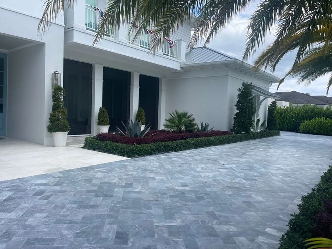 White house with dark windows, blue-gray brick driveway, manicured landscaping.
