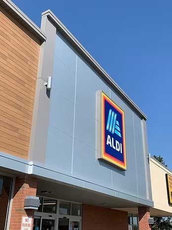 ALDI store exterior with large sign against a blue sky, gray and wood paneling, and a brick base.
