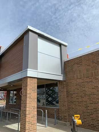 Building exterior with brick and silver panels, under a cloudy sky.