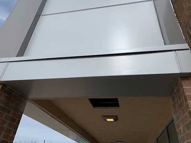 Exterior building with gray metal awning and white wall above; brick wall on the right.