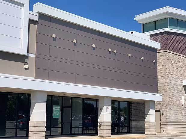 Exterior of a vacant commercial building with a brown facade, glass windows, and white trim.