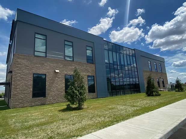 Modern two-story building with gray facade, brick accents, large windows, and manicured lawn under a blue sky.
